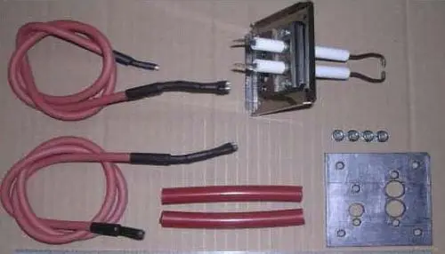 Zündeinheit von Remeha mit zwei elektrischen Zündkerzen, Kabeln, Schrauben und einer Metallplatte. Komponenten sind auf einem Karton angeordnet.